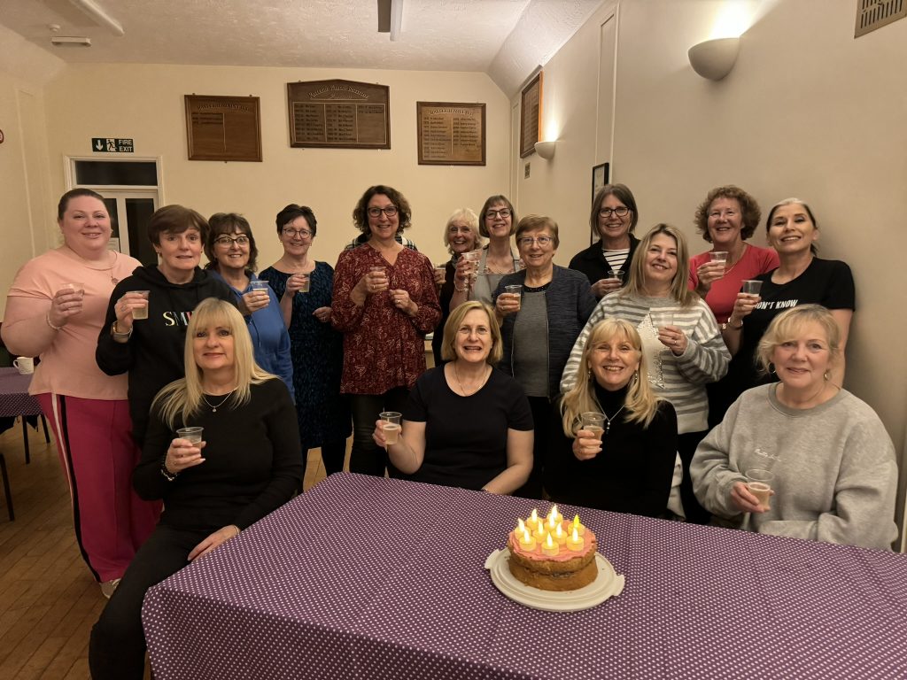 A group of ladies each with a glass of bubbly, and a birthday cake.